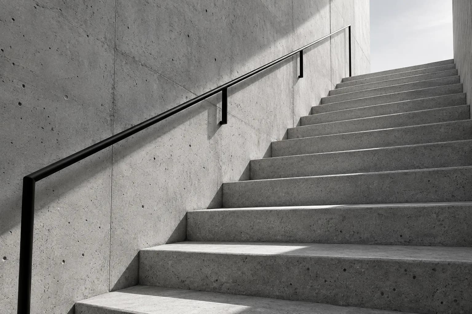 A concrete staircase rising toward daylight in a monochrome architectural study.